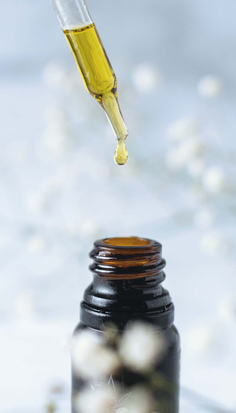 Hand with dropper removing CBD oil from bottle